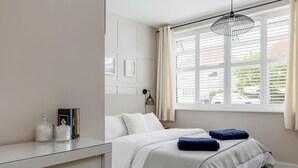 A bedroom with a bed, bedside table, and a window with blinds. - Modern 2bed Flat, Parking, Close to Beach & Shops (Bournemouth)