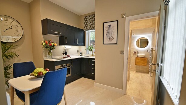 Une cuisine moderne avec des meubles de couleur sombre, une table à manger entourée de chaises bleues et une horloge au mur.
