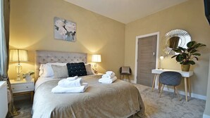 Une chambre d’hôtel avec un grand lit, une table de chevet avec une lampe, un bureau avec une chaise, un miroir et une plante en pot.