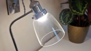 Une lampe de bureau avec un abat-jour transparent, une plante en pot et un élément décoratif circulaire fixé au mur.