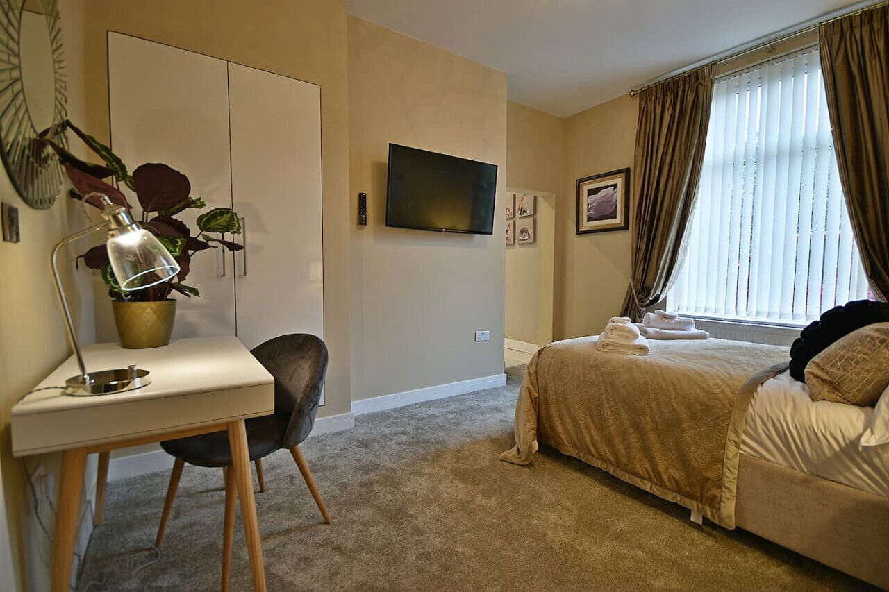 Habitación de hotel con cama, escritorio con lámpara, planta en maceta, televisor y ventana con cortinas.