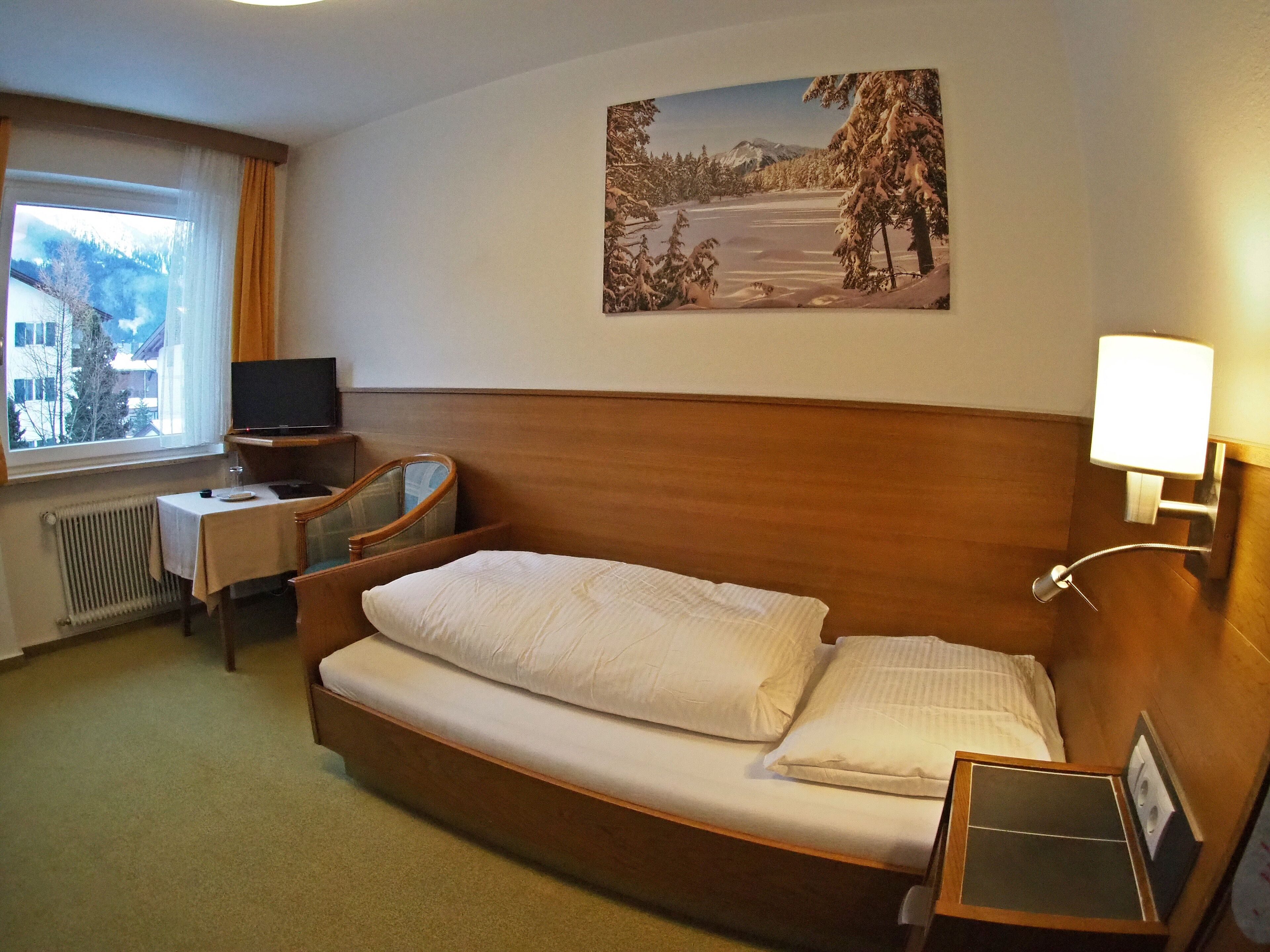 Una habitación de hotel con una cama, un escritorio con una silla, un televisor y un cuadro de un paisaje nevado.