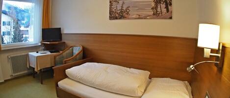 Una habitación de hotel con una cama, un escritorio con una silla, un televisor y un cuadro de un paisaje nevado.