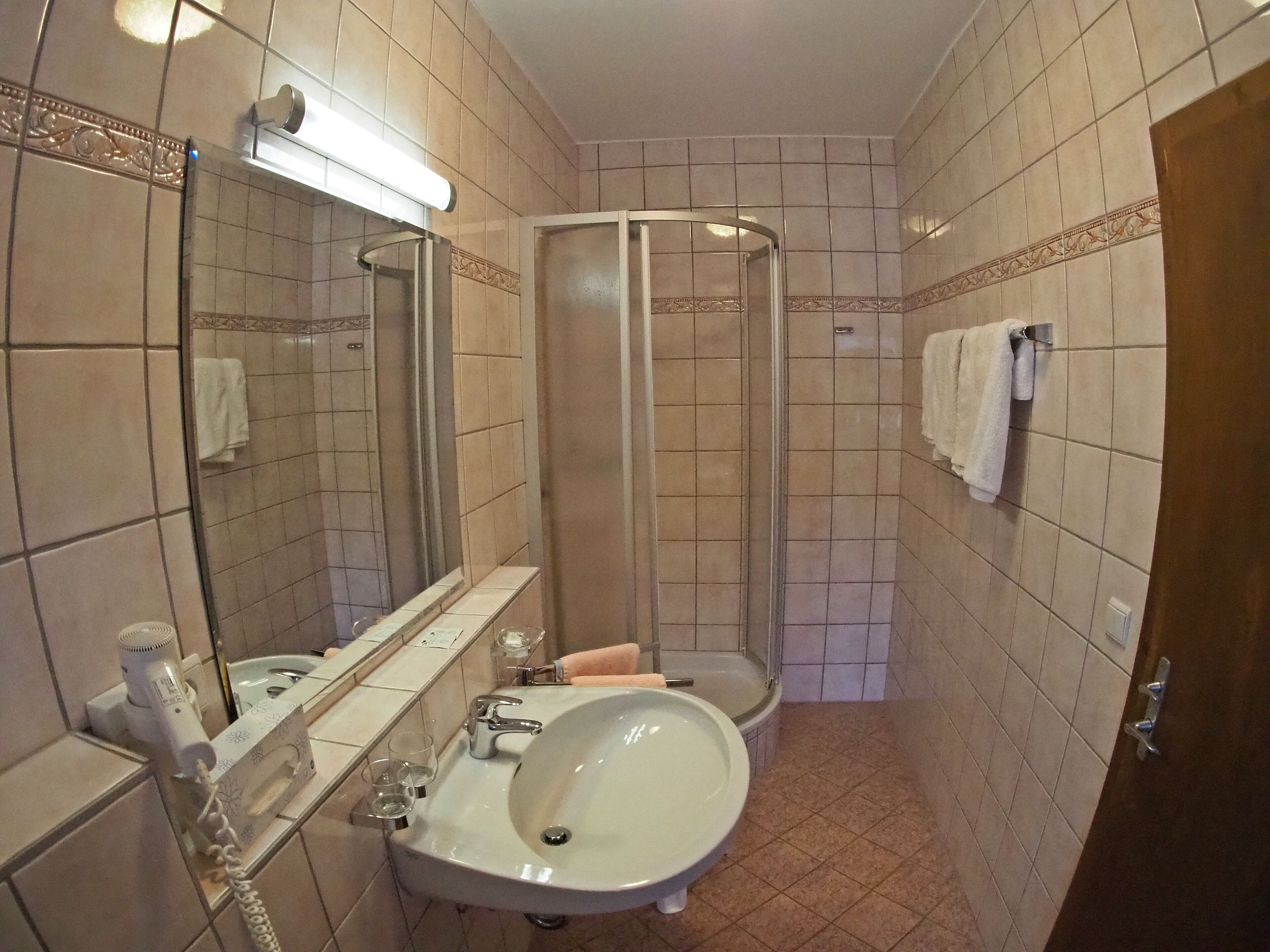 Baño con lavamanos, espejo, ducha y perchero para toallas.