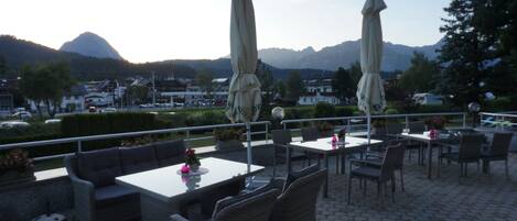 An outdoor patio area with tables and chairs, umbrellas, and a view of mountains in the background.