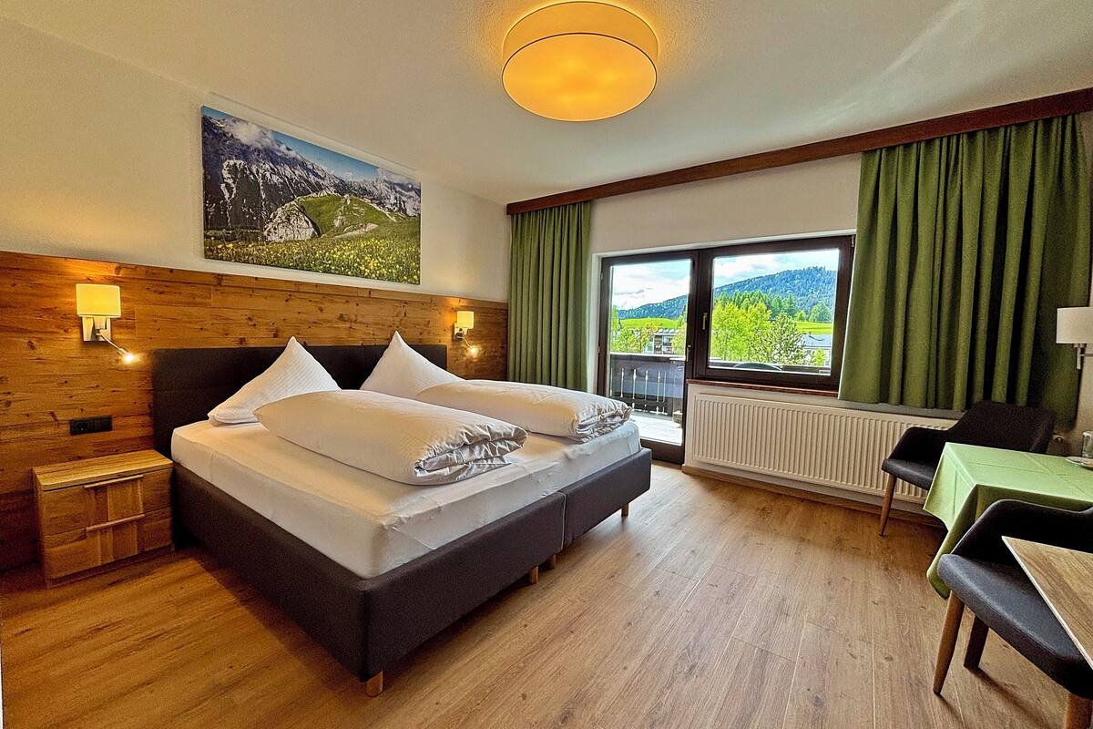 A hotel room with a bed, a view of the outdoors, a table, and a chair.