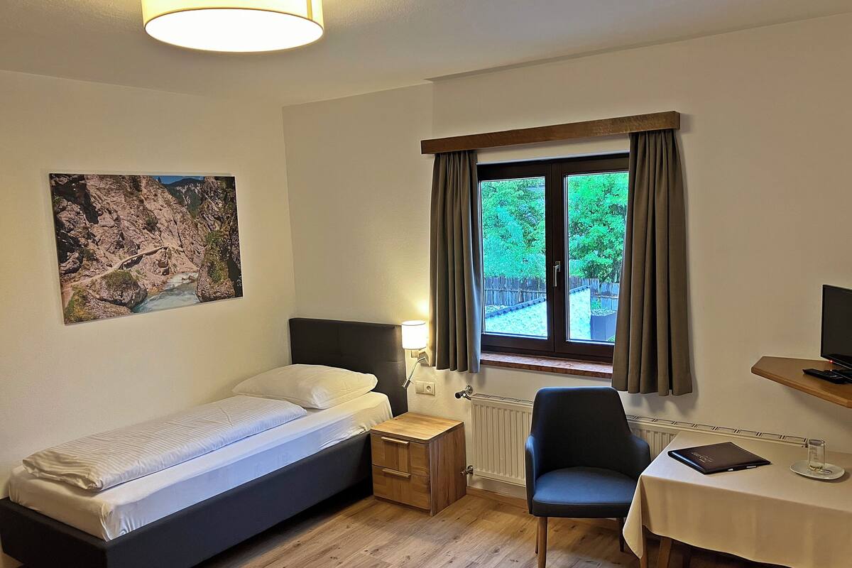 A bedroom with a bed, bedside table, chair, desk, and a window with curtains.