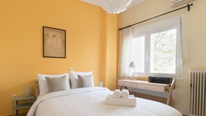 A neatly arranged bedroom with a large bed, a bedside table, a window with curtains, and a radiator. - Tati's Parthenon apt 2bdr/1,5bthr/100Mbps VDSL- 5mins walk to Acropolis (Αθήνα)