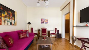 A living room with a vibrant pink sofa, a wooden coffee table, and a dining area with a glass table and chairs. - Tati's Parthenon apt 2bdr/1,5bthr/100Mbps VDSL- 5mins walk to Acropolis (Αθήνα)
