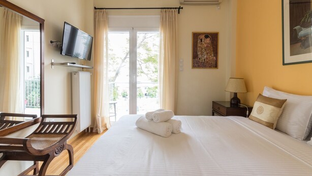 A hotel room with a bed, a TV mounted on the wall, a painting, and a window with curtains. - Tati's Parthenon apt 2bdr/1,5bthr/100Mbps VDSL- 5mins walk to Acropolis (Αθήνα)