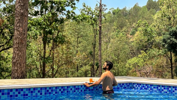 Un hombre en una piscina con borde de azulejos, rodeado de árboles.