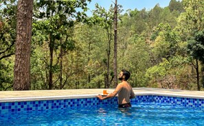 Un homme dans une piscine dont le bord est recouvert de carreaux, entourée d’arbres.