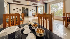 Un comedor con mesas y sillas de madera, una barra de buffet con recipientes llenos de comida, y vistas a árboles a través de grandes ventanales.