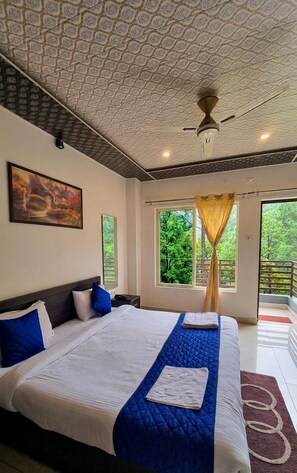 A hotel room with a large bed, a ceiling fan, a painting on the wall, and a window with curtains. - Pine Valley Gold Resort (Lansdowne)
