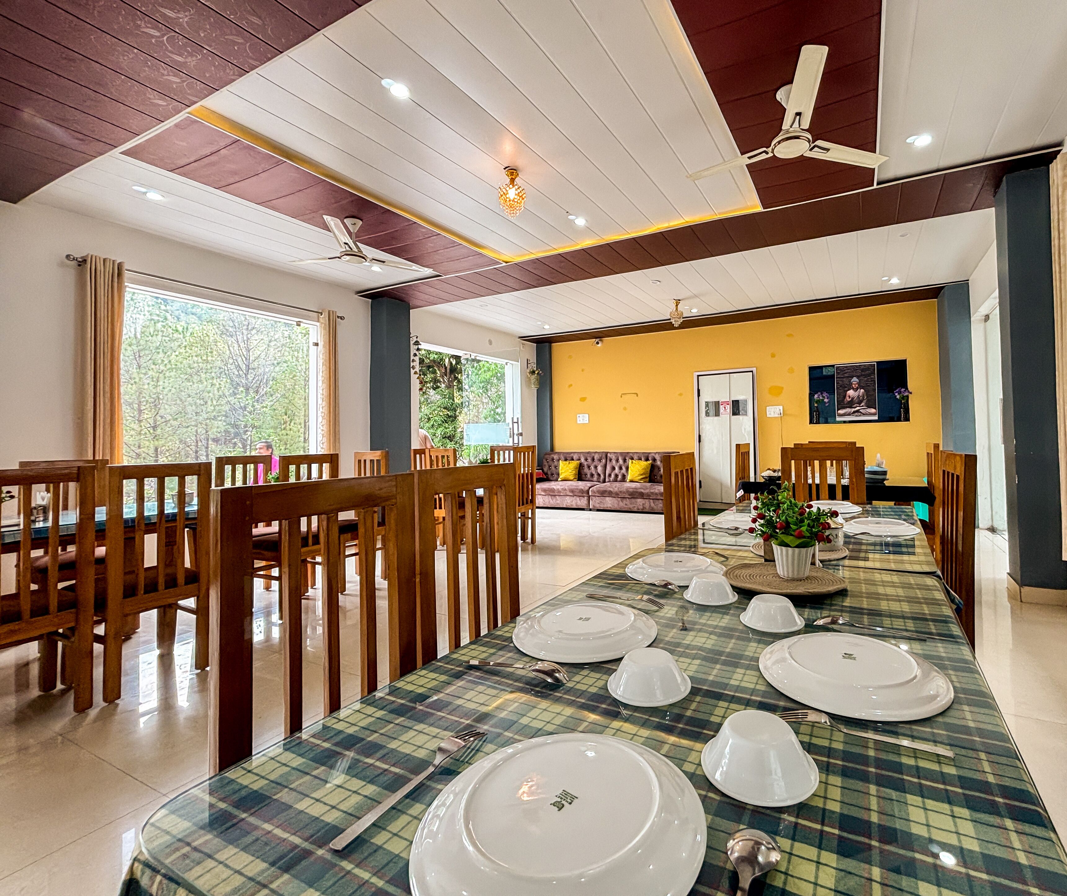 A dining area with a long table set for multiple guests, wooden chairs, ceiling fans, and a yellow accent wall.