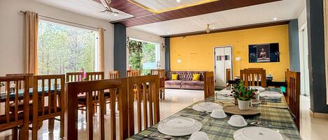 A dining area with a long table set for multiple guests, wooden chairs, ceiling fans, and a yellow accent wall.