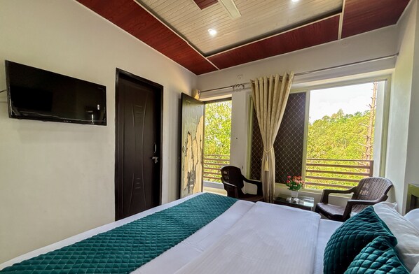 Une chambre d’hôtel avec un lit, un téléviseur fixé au mur, une fenêtre avec des rideaux et une vue sur la verdure.