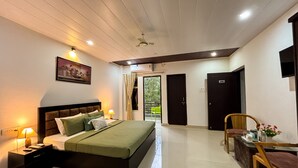 Habitación de hotel con cama, mesita de noche, lámpara y vistas al exterior.
