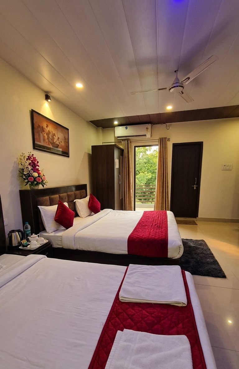A hotel room with two beds, a painting, a vase of flowers, and a view of the outdoors.