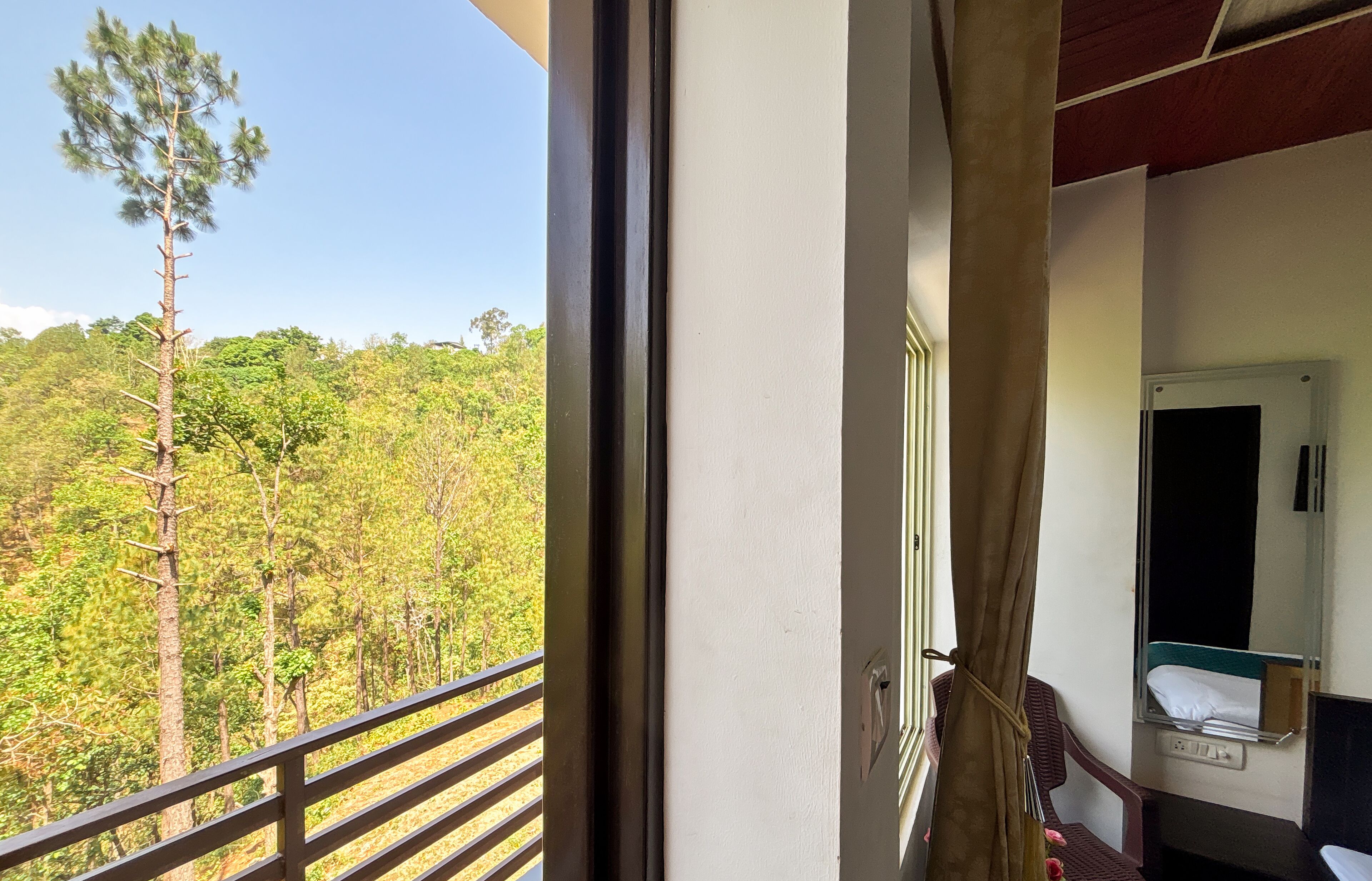 A room with a window overlooking a forested area, a bed, and a small table with a chair.