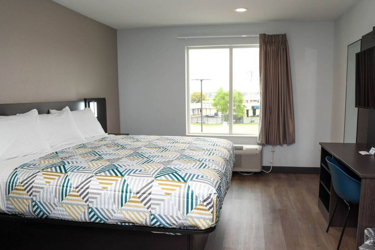 A hotel room with a bed, a desk, a chair, a television, and a window with curtains.