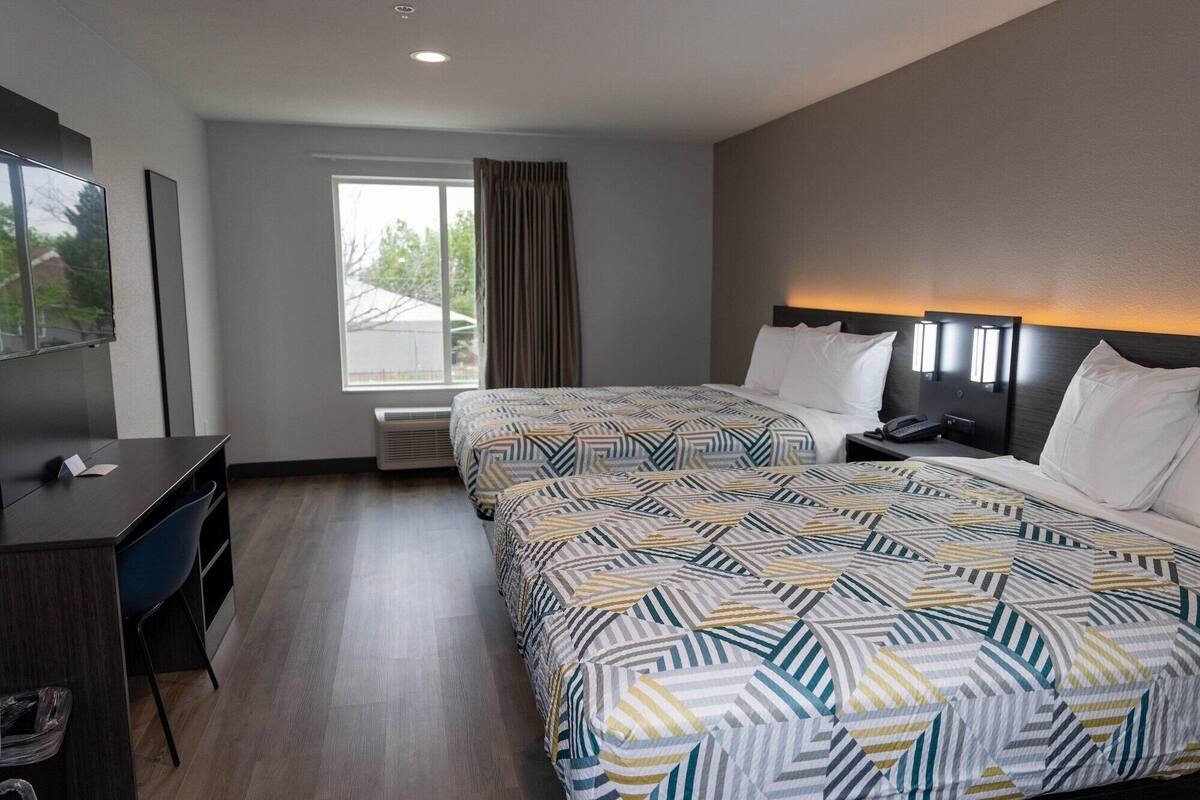 A hotel room with two beds, a desk, a chair, a TV, and a window with curtains.