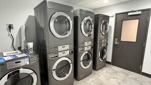 A laundry facility with three stacked front-loading washing machines, a control panel, and a door with a window. - Motel 6 Fort Worth, TX - Lake Worth (Fort Worth)