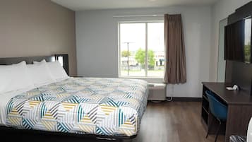 A hotel room with a bed, a desk, a chair, a TV, and a window with curtains.