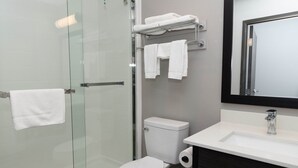 A modern bathroom with a glass shower enclosure, a white toilet, a sink with a mirror, and towels on a rack. - Motel 6 Fort Worth, TX - Lake Worth (Fort Worth)