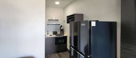 Una kitchenette compacta con un refrigerador negro, un microondas, una cafetera y un tostador.