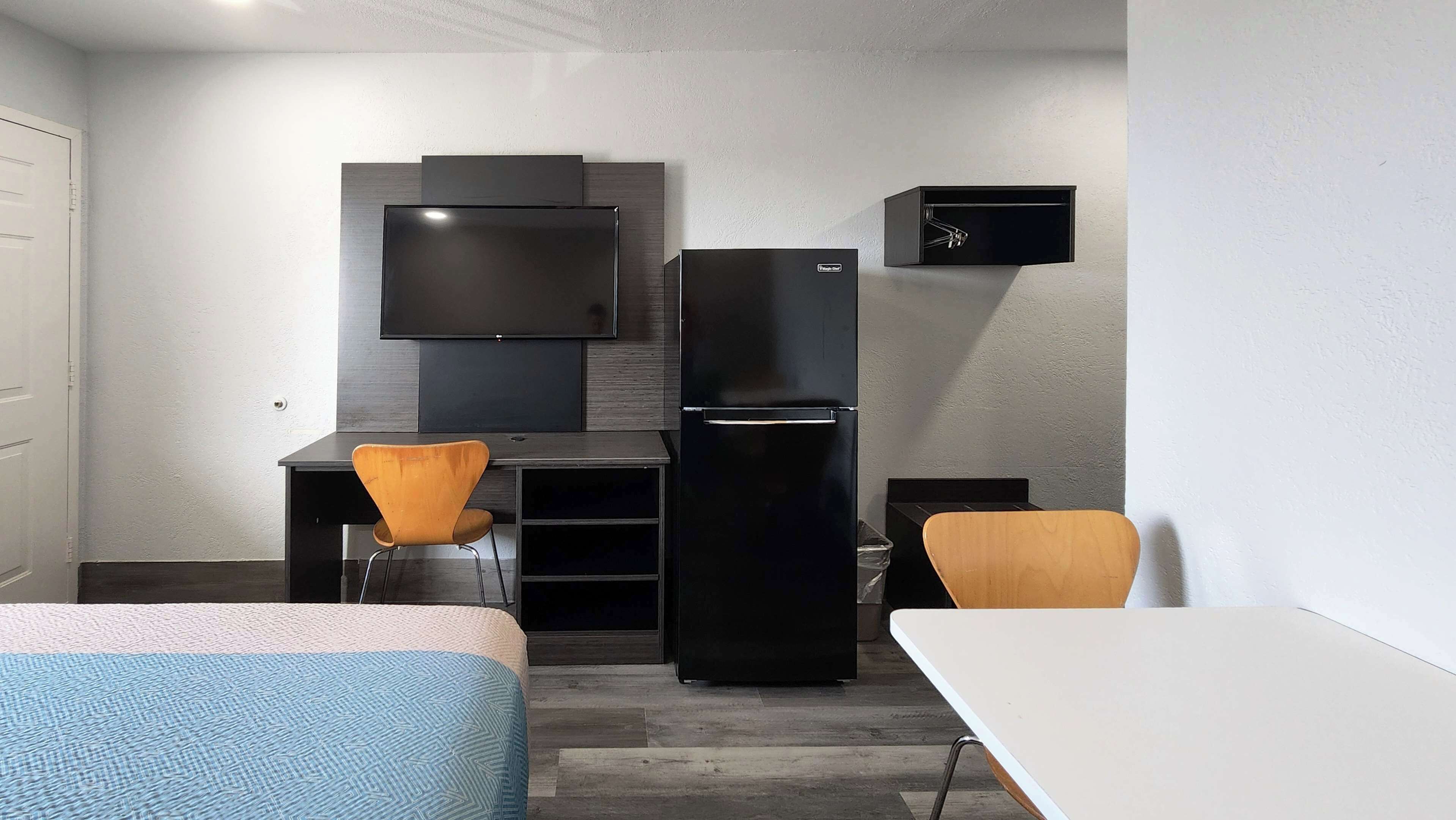 Quarto de hotel pequeno com cama, escrivaninha, cadeira, televisão, frigorífico e armário.
