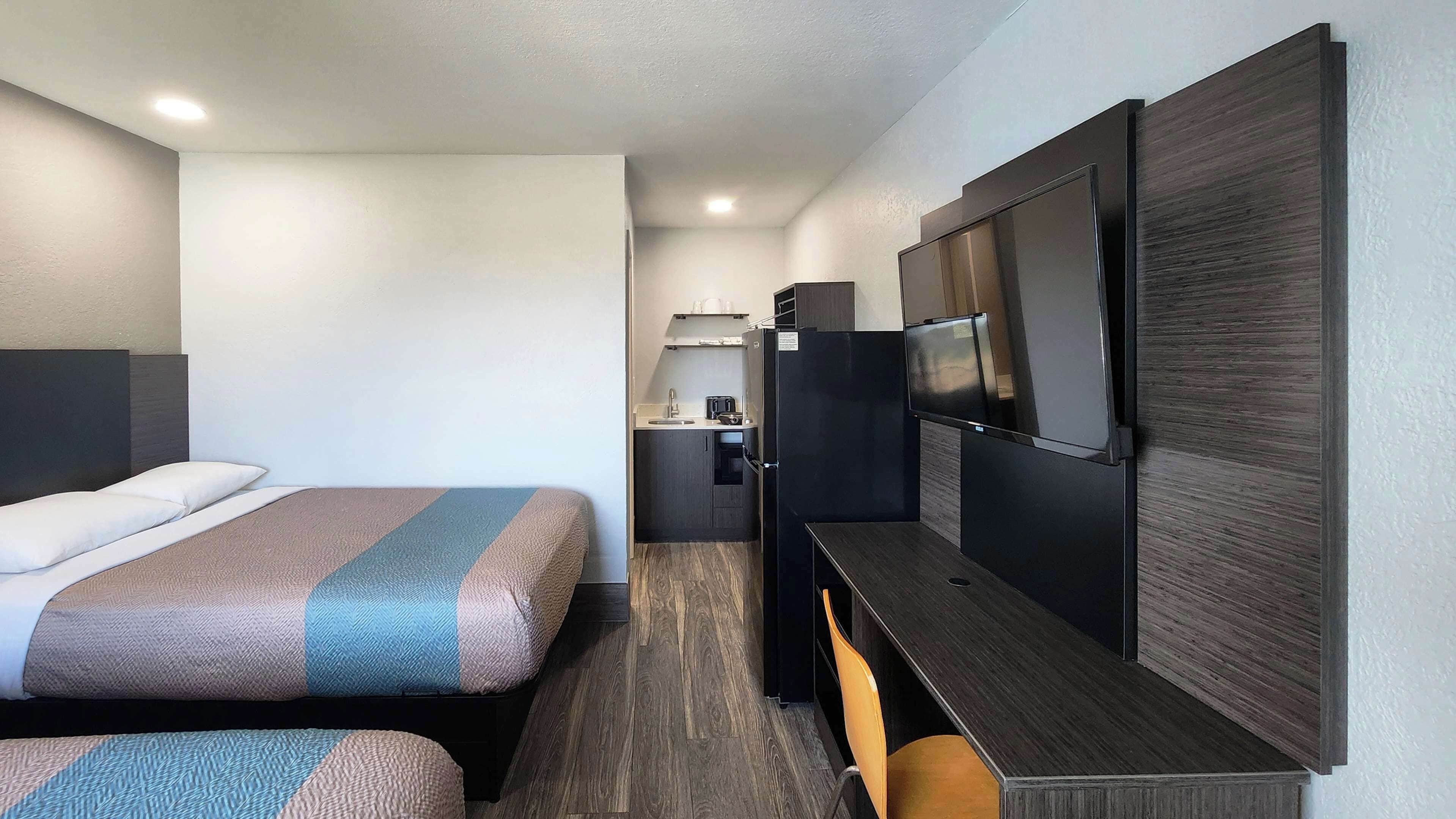 A hotel room with a bed, a desk, a TV, and a kitchenette.
