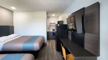 A hotel room with a bed, a desk, a TV, and a kitchenette.