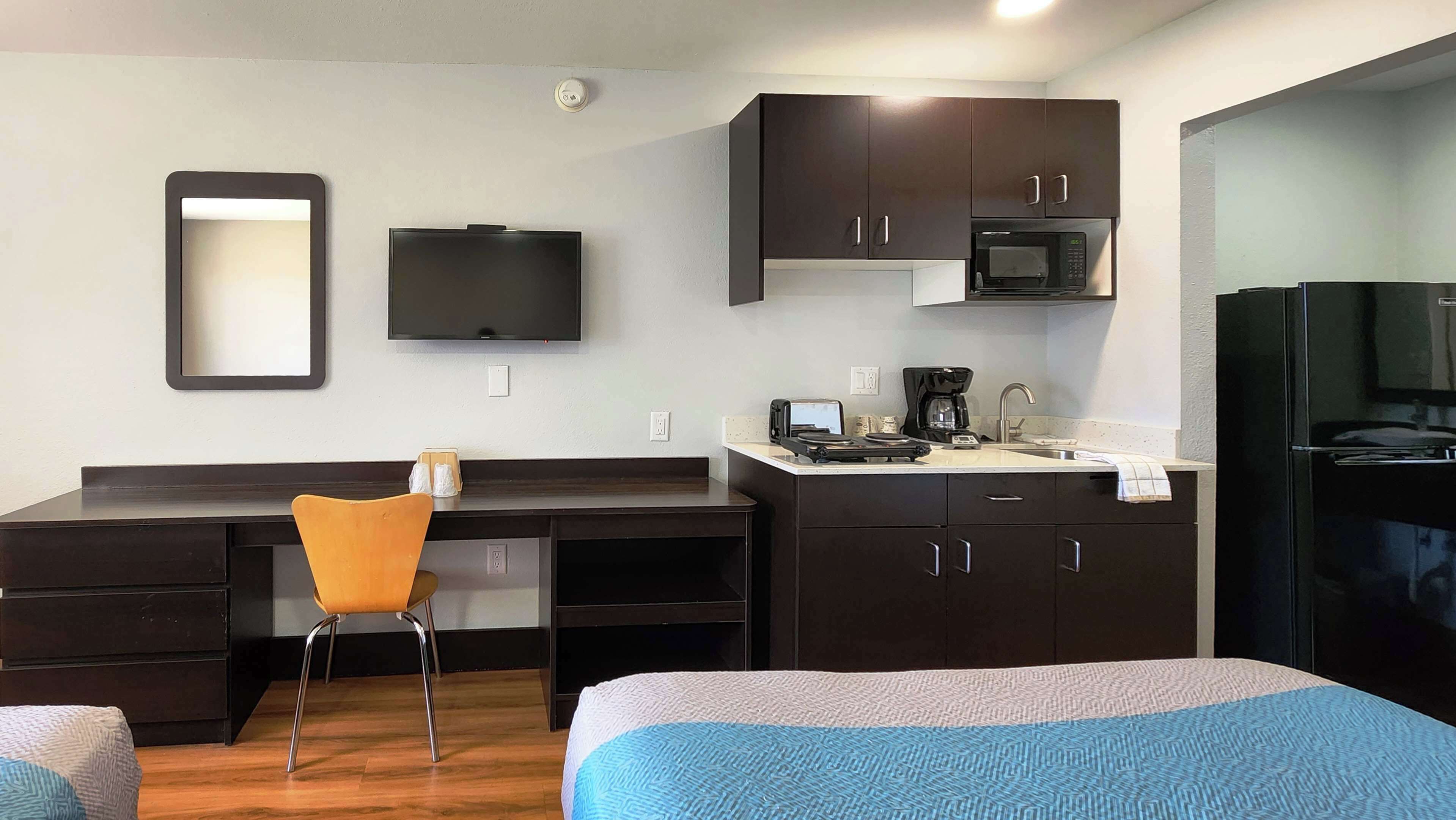 Une chambre d’hôtel compacte comprenant un coin cuisine, un téléviseur à écran plat, un four à micro-ondes, un réfrigérateur, un bureau avec une chaise et deux lits avec une literie bleue.
