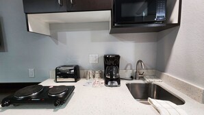 A kitchenette with a microwave, toaster, coffee maker, and a sink. - Studio 6 Webster, TX Houston - NASA Lake (Webster)