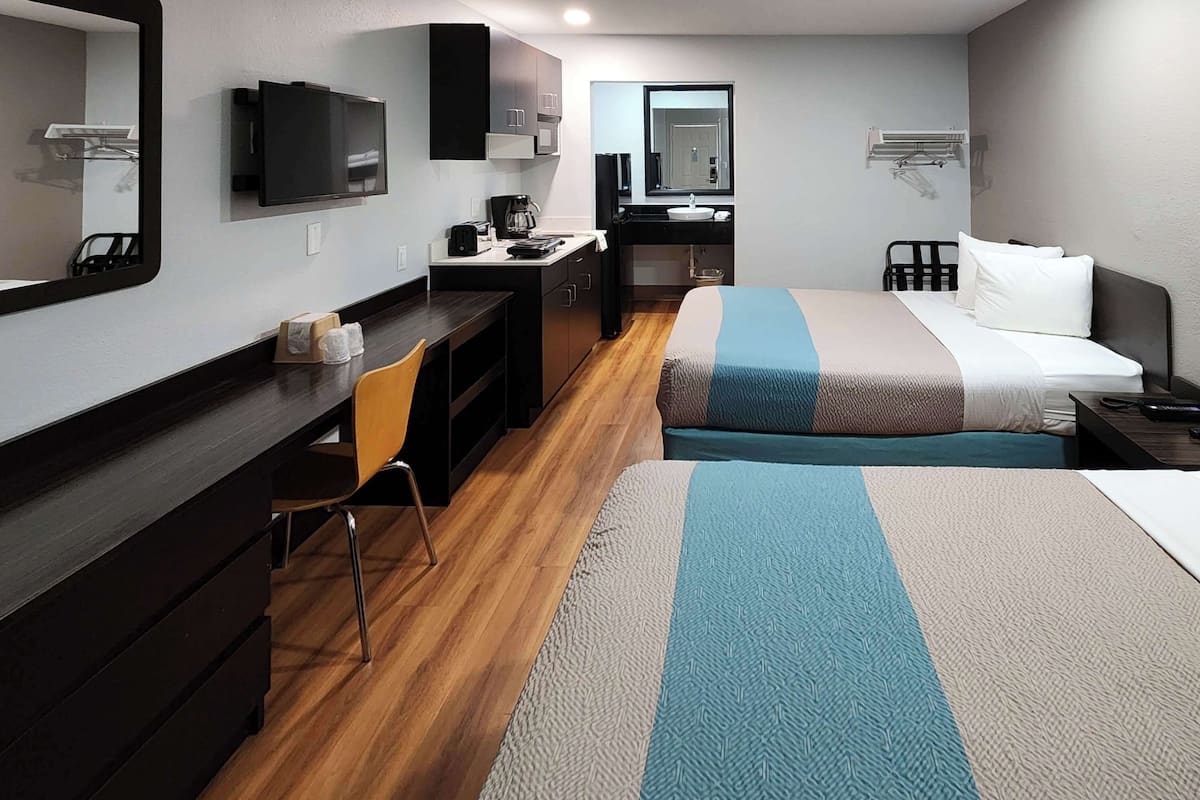 A hotel room with a desk, chair, bed, and a television.