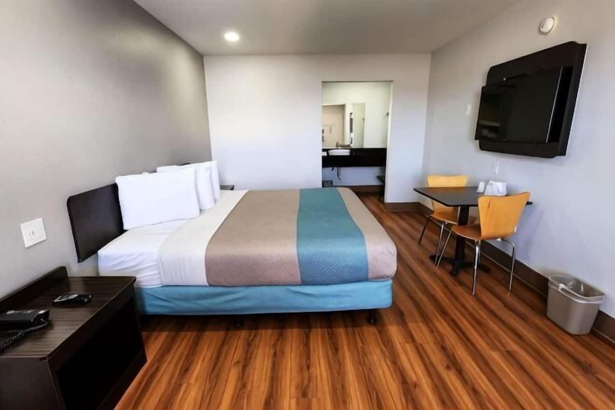 A hotel room with a bed, a desk, a chair, a TV, and a trash bin.