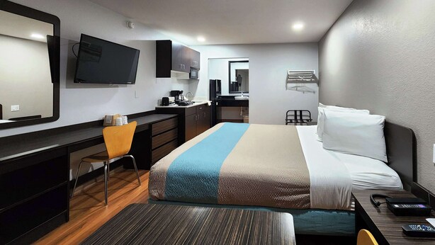A hotel room with a bed, a desk, a chair, a TV, a microwave, a sink, and a mirror. - Studio 6 Webster, TX Houston - NASA Lake (Webster)
