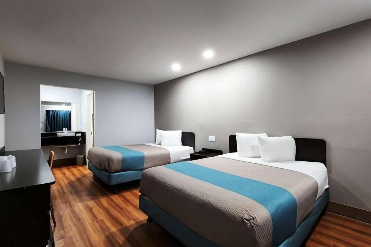 A hotel room with two beds, a desk, a chair, and a mirror.
