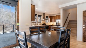 A modern kitchen with wooden cabinets, a dining table with chairs, and a view of the outdoors. - Open-Concept Townhome Next to Blue River w/ Private Wrap-Around Patio! (Silverthorne)