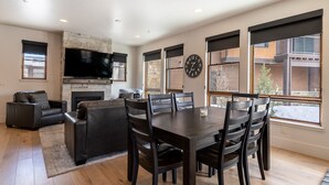 A modern living room with a fireplace, a large flat-screen TV, and a dining area with a table and chairs. - Open-Concept Townhome Next to Blue River w/ Private Wrap-Around Patio! (Silverthorne)