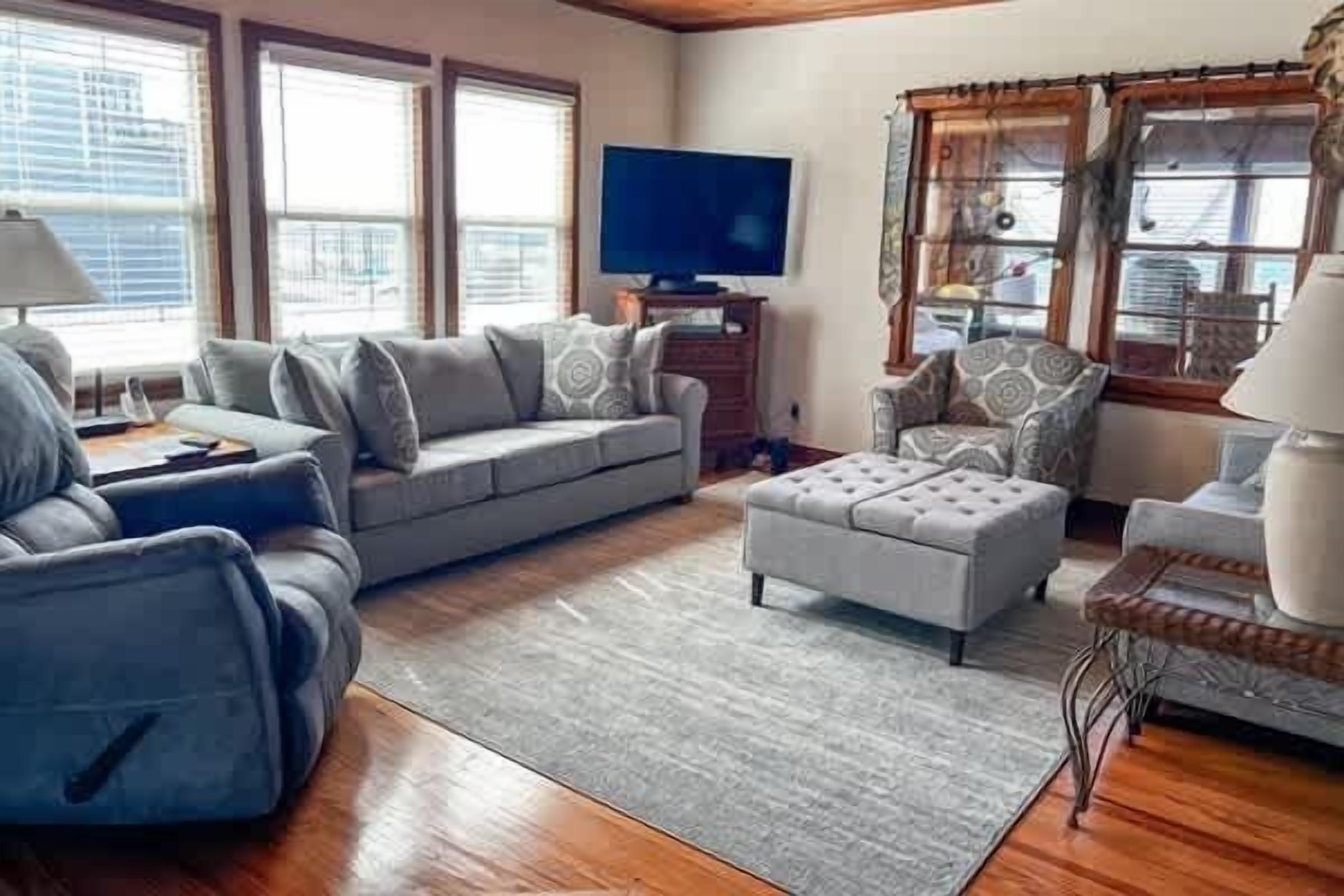 A living room with a sofa, ottoman, and armchairs, a television, and a window with blinds.