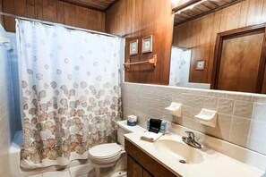 A bathroom with a shower curtain, toilet, sink, and mirror. - Beachfront Coastal Cottage St George Island (St.George Island)