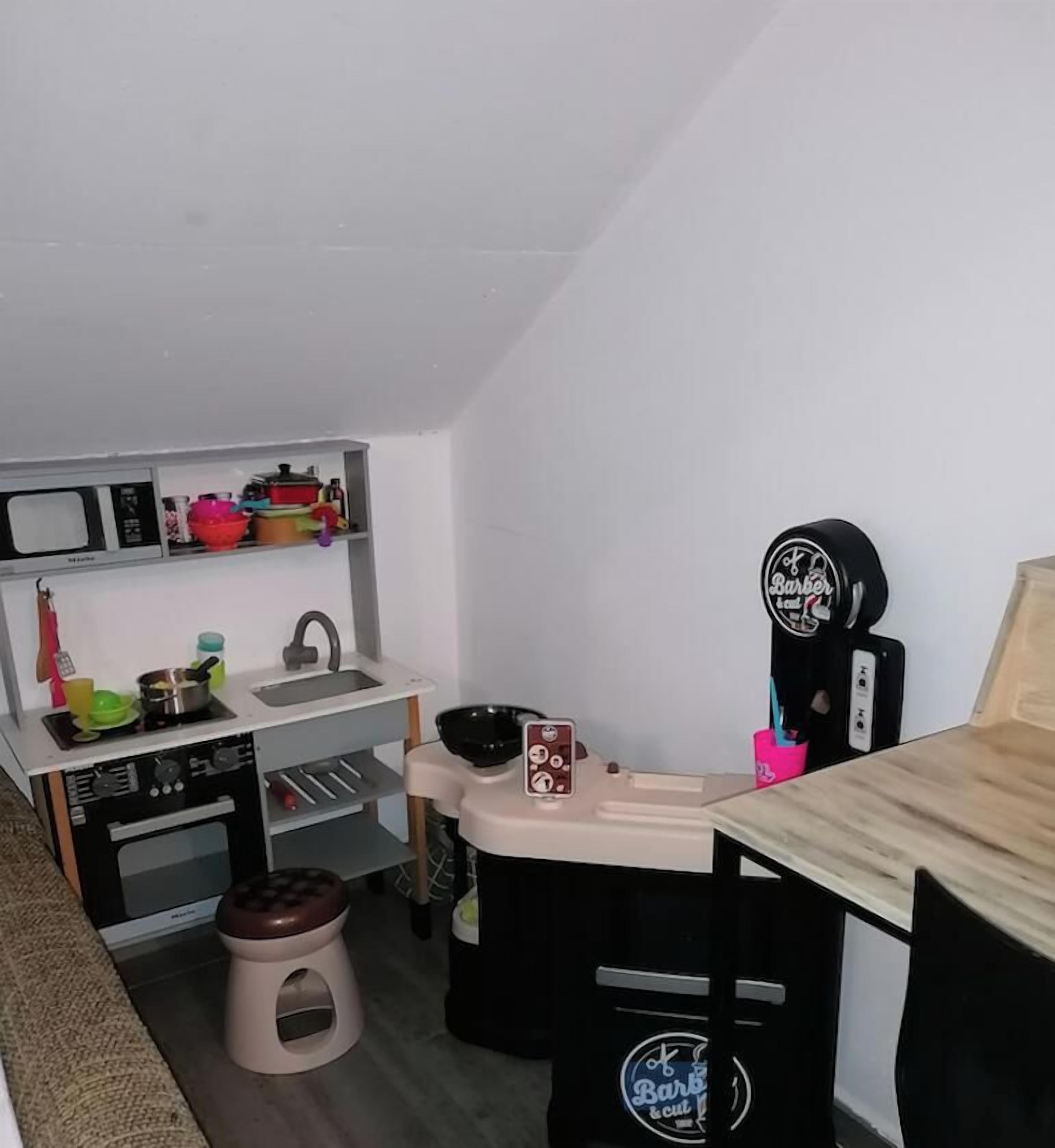 Een kleine keuken met een magnetron, spoelbak en een klein oven. Er is een kruk en een tafel met een koffieapparaat.