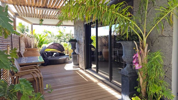 Une terrasse extérieure avec une plateforme en bois, des meubles en osier et des plantes en pot.
