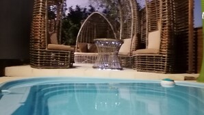 Une piscine entourée de meubles en osier et agrémentée d’une table en verre au centre.
