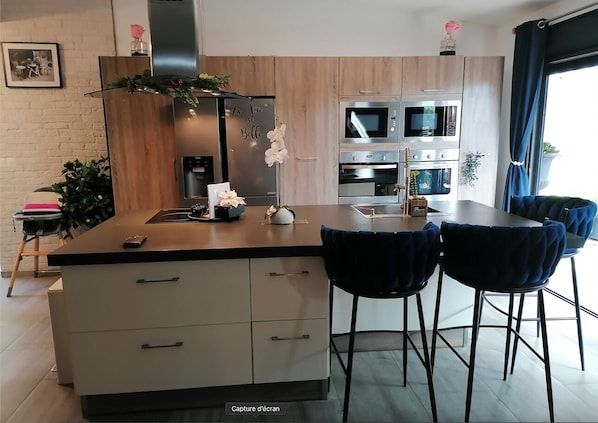 Una cocina moderna con una isla central, dos hornos, un microondas y un comedor con cuatro sillas.