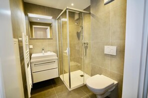 A modern bathroom with a glass-enclosed shower, a white sink, and a toilet.