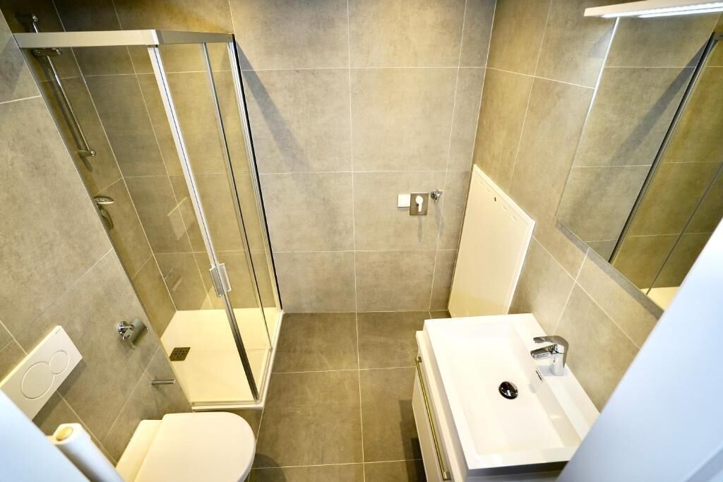 Een moderne badkamer met een douchecabine van glas, een witte wastafel en een toilet.
