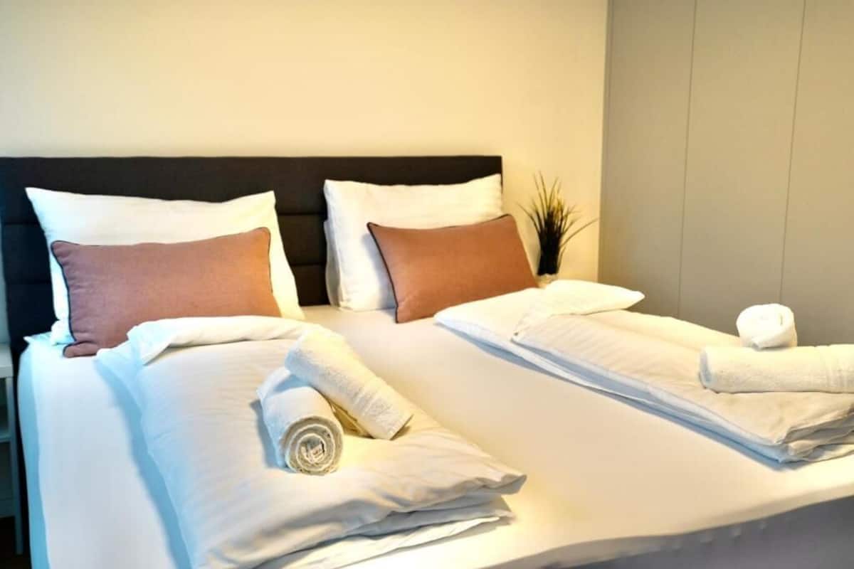 Et hotelværelse med to senge, begge med hvide hør og brune puder. Der er sammenrullede håndklæder på sengene.